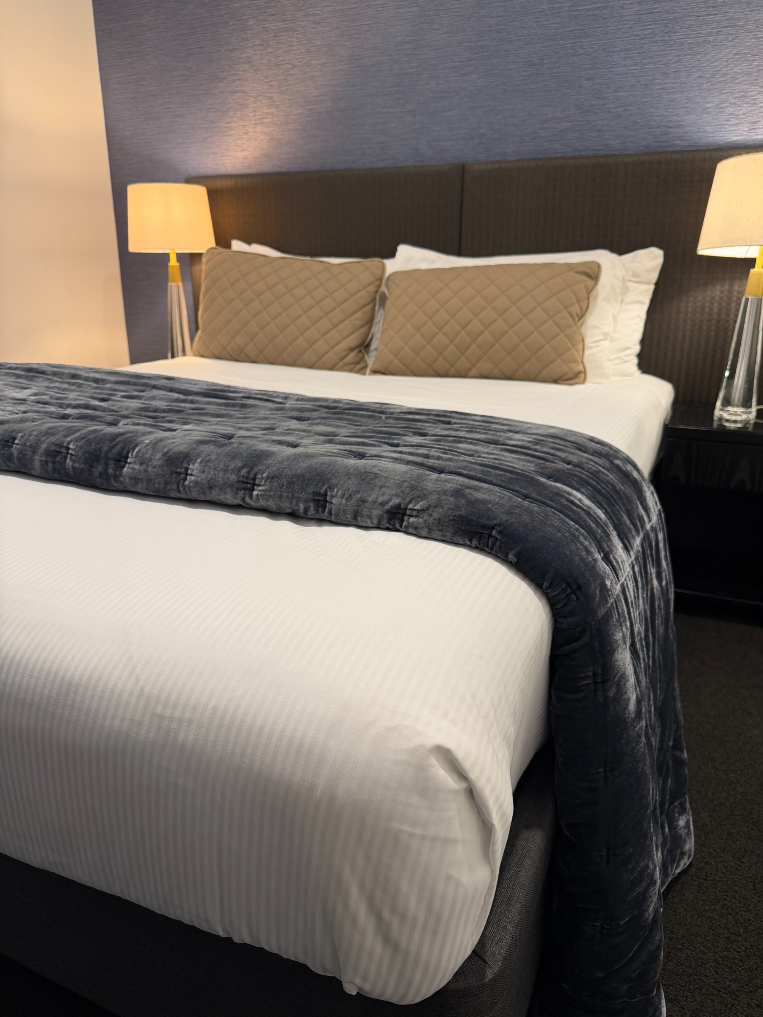 A neatly made hotel bed with white sheets, pillows and a charcoal throw